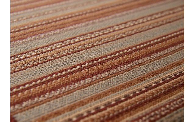 Gros plan sur un tapis tissé à la hand, montrant la richesse des textures et les motifs géométriques subtils dans des tons terreux.